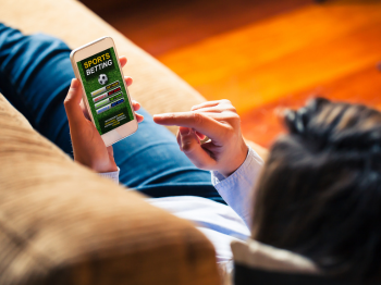 Woman holding a mobile phone to visit a sports betting website while lies down at home